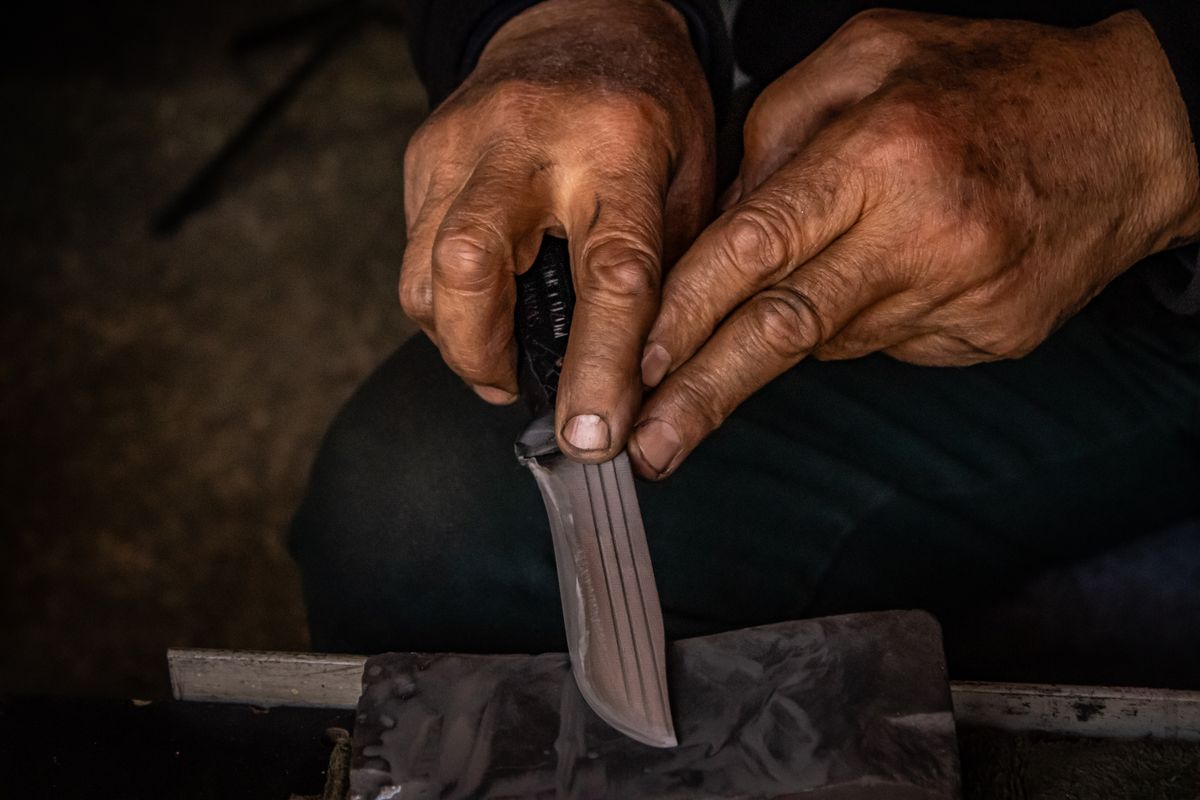 Unas manos afilan la hoja de un cuchillo de cocina sobre una piedra oscura.