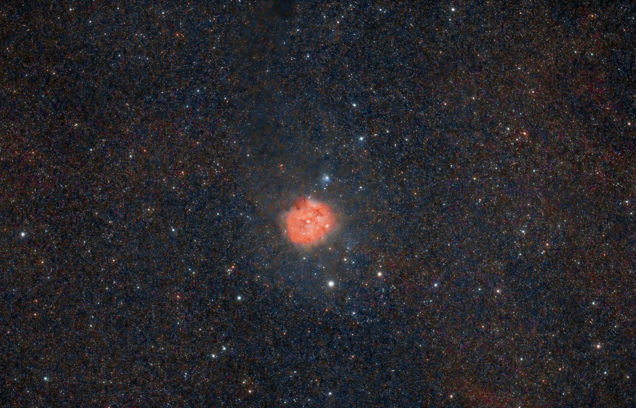Campo de estrellas nocturno con una nebulosa rojiza en el centro, rodeada de miles de puntos de luz sobre fondo oscuro