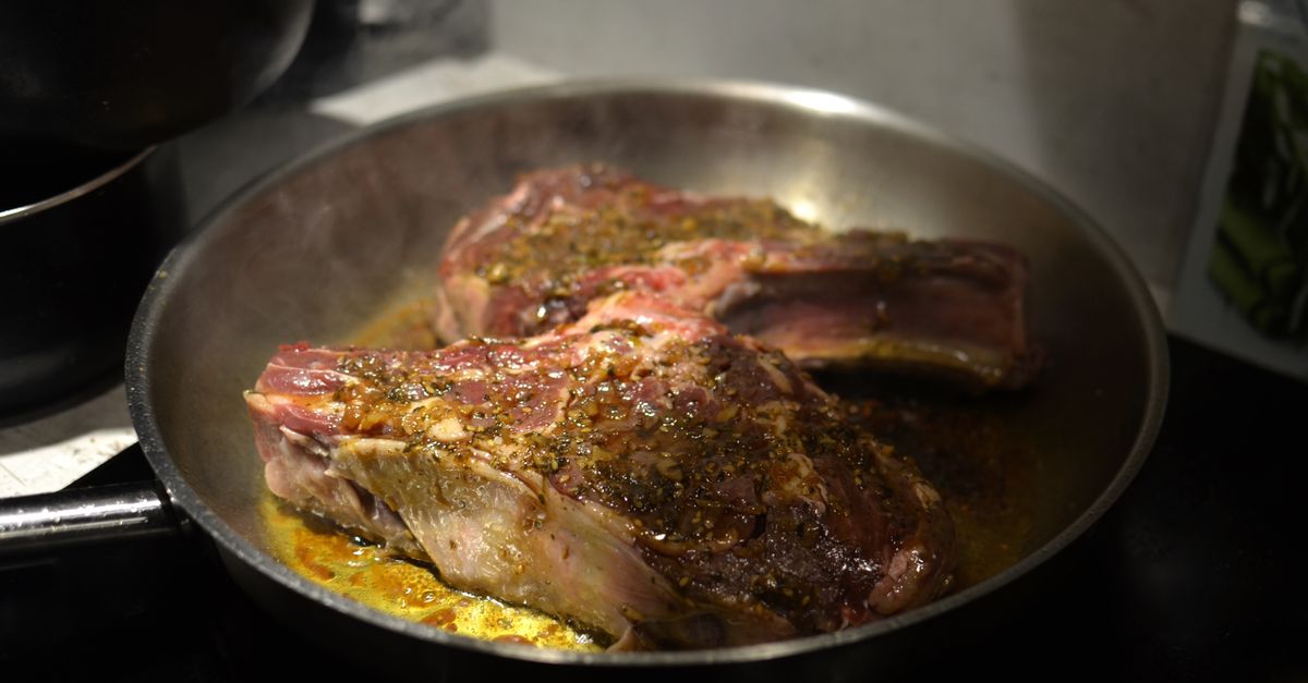 Chuletas de cordero cocinándose en una sartén de metal sobre el fuego, en contacto directo con la superficie caliente