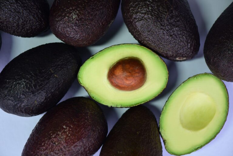 Aguacates enteros junto a mitades cortadas que muestran su pulpa verde y el hueso, el punto de partida para aplicar el truco de la cebolla.