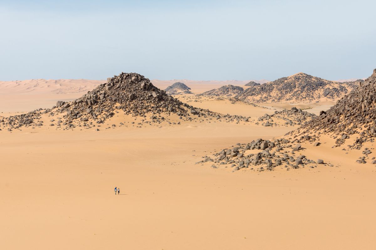 Paisaje desértico de Bir Tawil, con colinas rocosas y dos personas caminando entre las dunas.