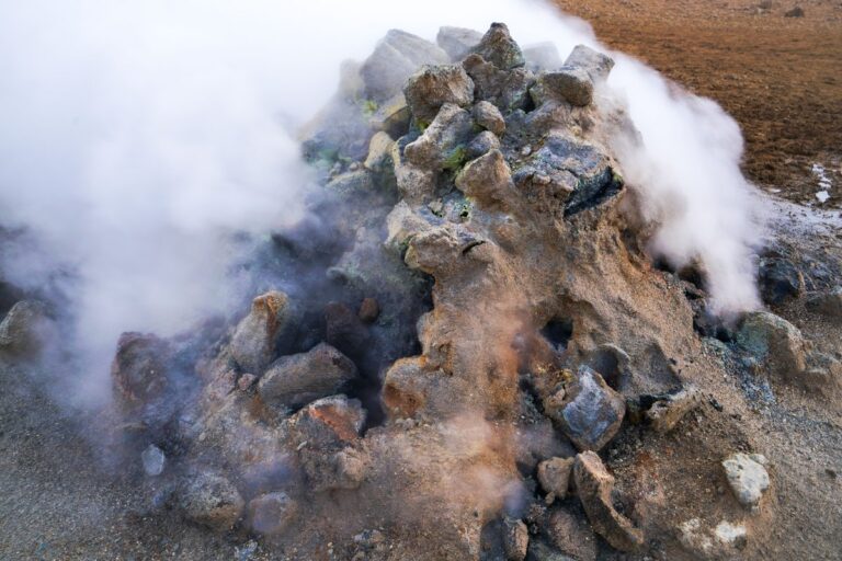 Humo y vapor blanco saliendo entre grietas de rocas con depósitos de azufre amarillento, señal de calor y combustión bajo tierra.