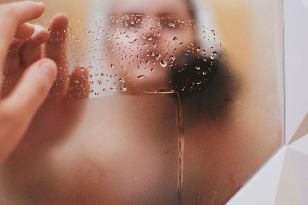 Espejo del baño cubierto de vaho y gotas de agua, con una mano rozando el cristal empañado.