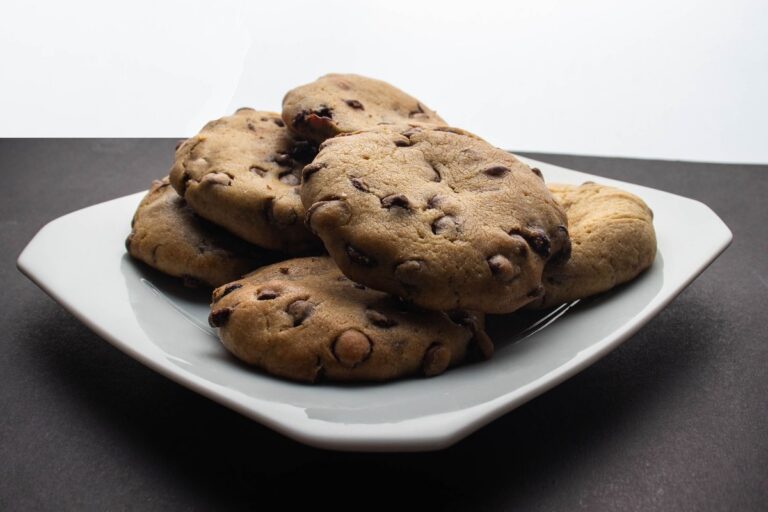 Galletas con pepitas de chocolate apiladas en un plato blanco cuadrado sobre una superficie oscura.