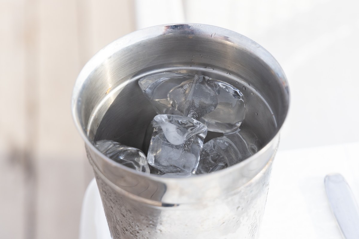 Cubitos de hielo flotando en agua dentro de un vaso metálico, como el que se usa en el truco de la moneda congelada.